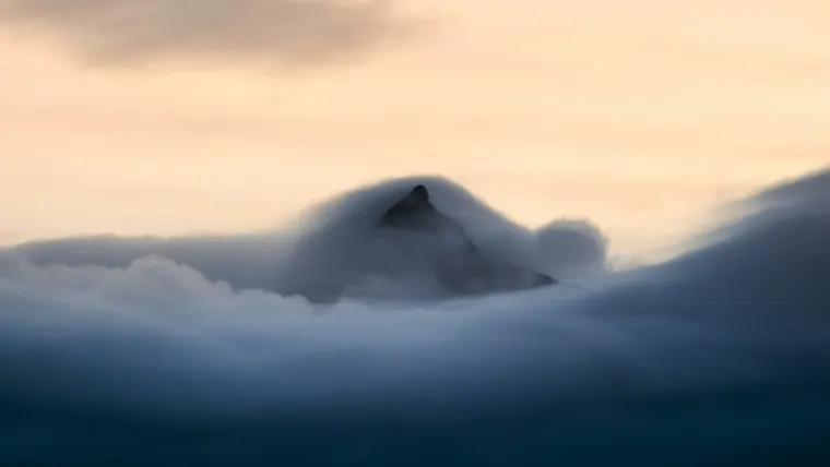 A lone mountain peak emerging from swirling clouds at dawn