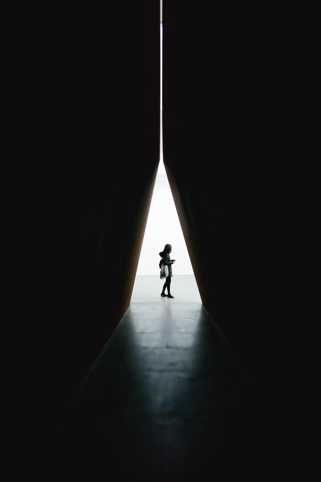 A lone figure standing in a narrow shaft of light between two towering dark walls